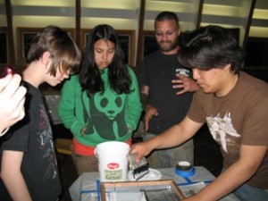 (L to R) Emily Grenier and Toney Gooday-Ervin learn about silk-screening from Matt Wiedenheft, a co-founder of YouthPeace and an artist who created the designs, while Dan Park works the screen.